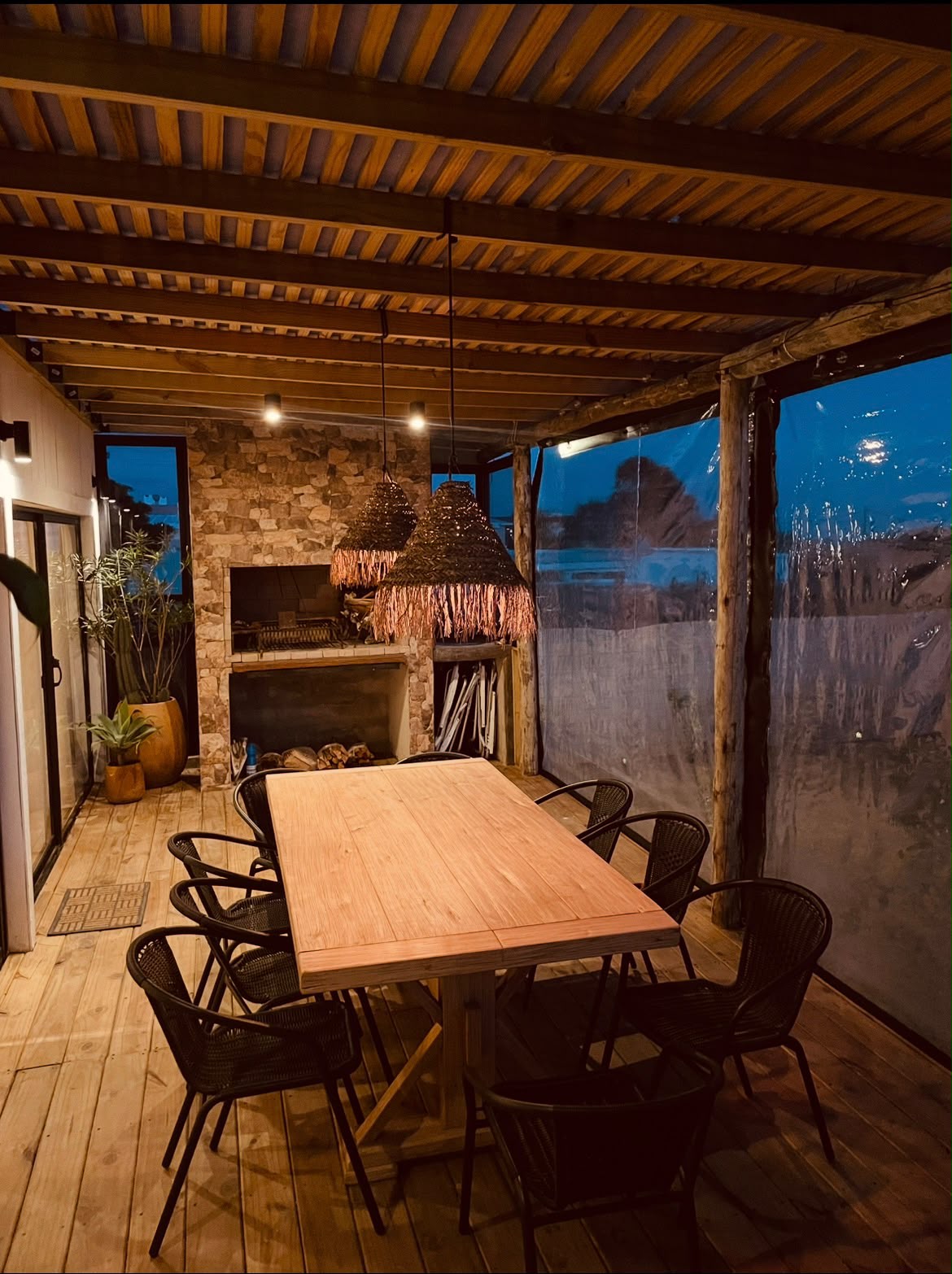 Deck cerrado con cortinas, mesa larga y parrillero de piedra